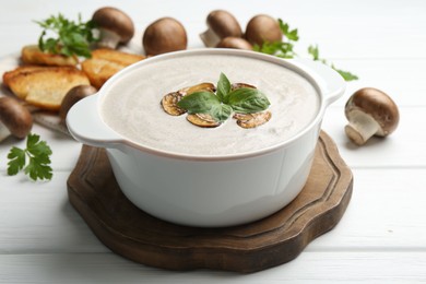 Delicious homemade mushroom soup in ceramic pot, croutons, fresh champignons and parsley on white wooden table