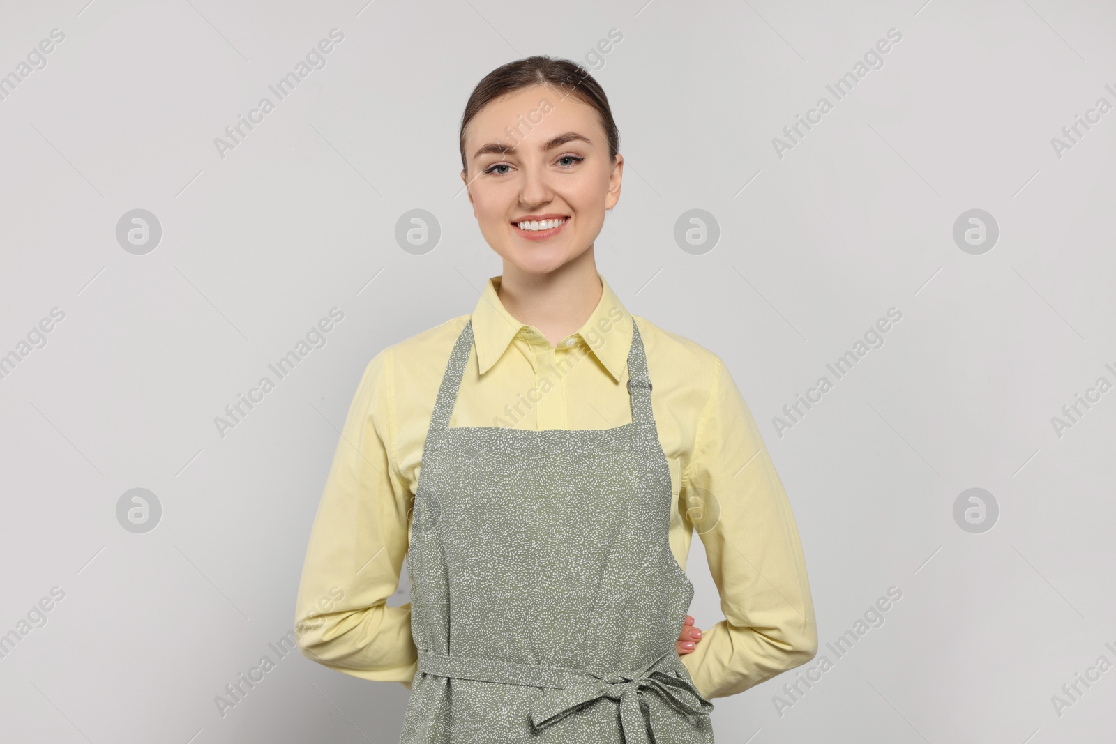 Photo of Beautiful young woman in clean apron with pattern on light grey background