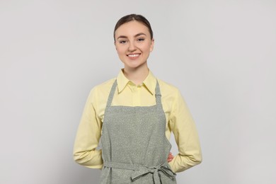 Beautiful young woman in clean apron with pattern on light grey background