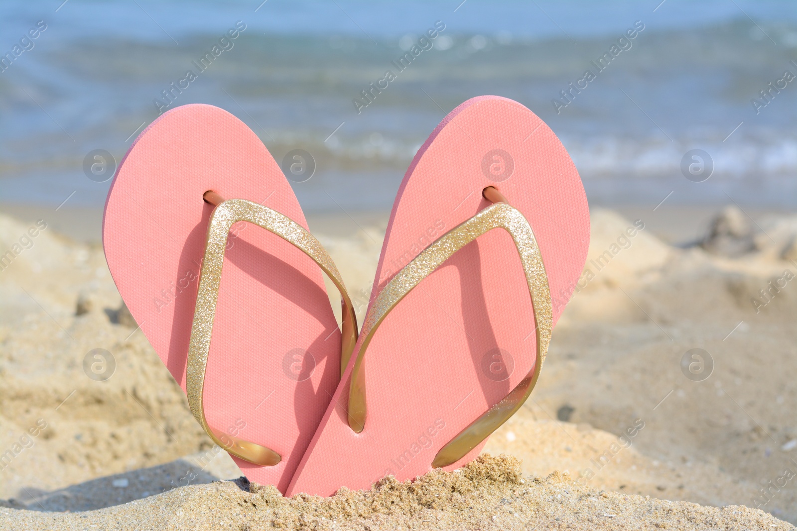 Photo of Stylish flip flops in sand on beach near sea