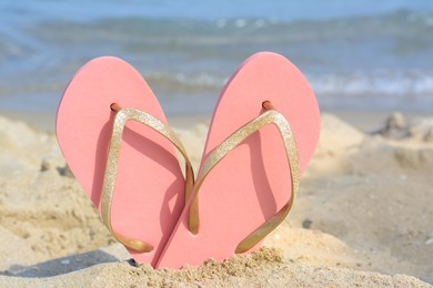 Stylish flip flops in sand on beach near sea