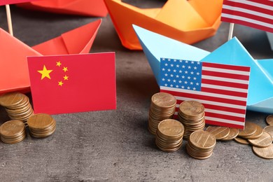 Photo of American and Chinese flags, coins with paper boats on grey table. Trade war concept