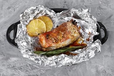 Tasty pork baked in foil, rosemary and lemon slices on grey textured table, top view