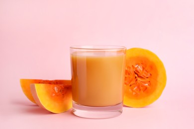 Tasty pumpkin juice in glass and cut pumpkin on pink background