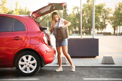 Photo of Young pregnant woman with bag talking on phone near car trunk outdoors