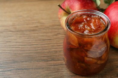 Tasty apple jam in glass jar and fresh fruits on wooden table, closeup. Space for text