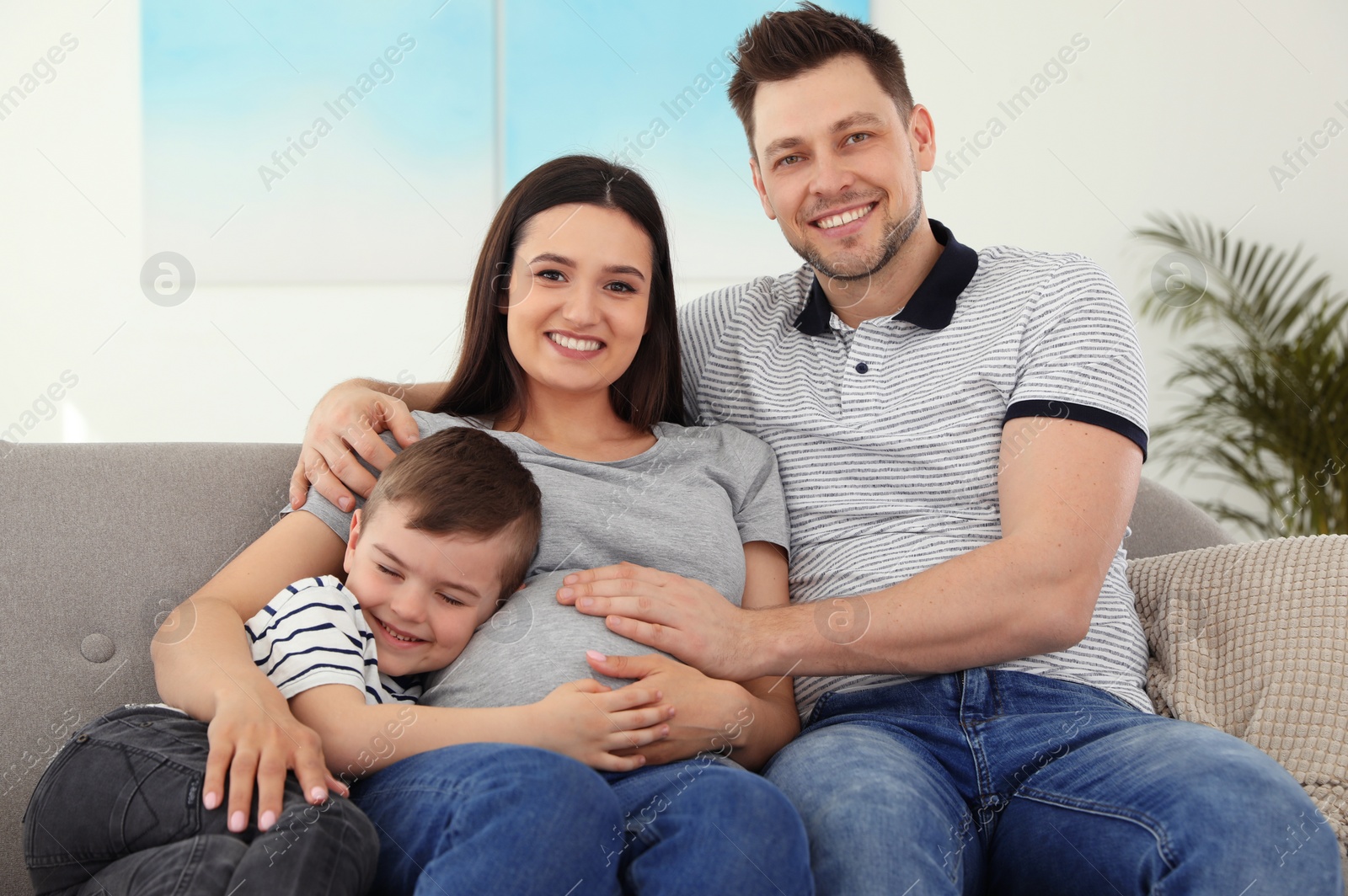 Photo of Father, son and pregnant mother spending time together on sofa at home. Family time