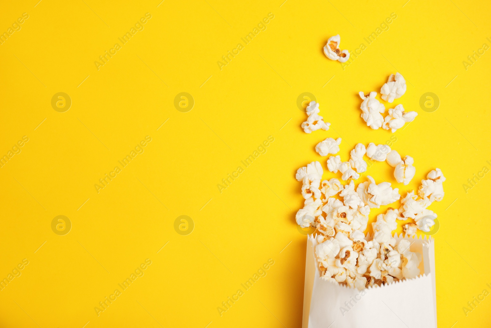 Photo of Paper bag with tasty fresh popcorn on color background, top view