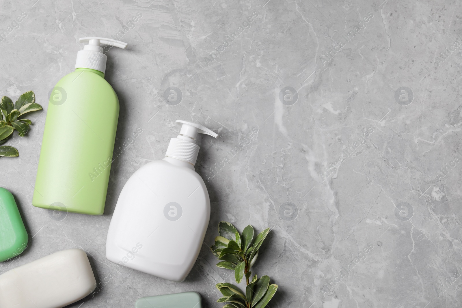 Photo of Different soap bars, bottle dispensers and green plants on light grey table, flat lay. Space for text