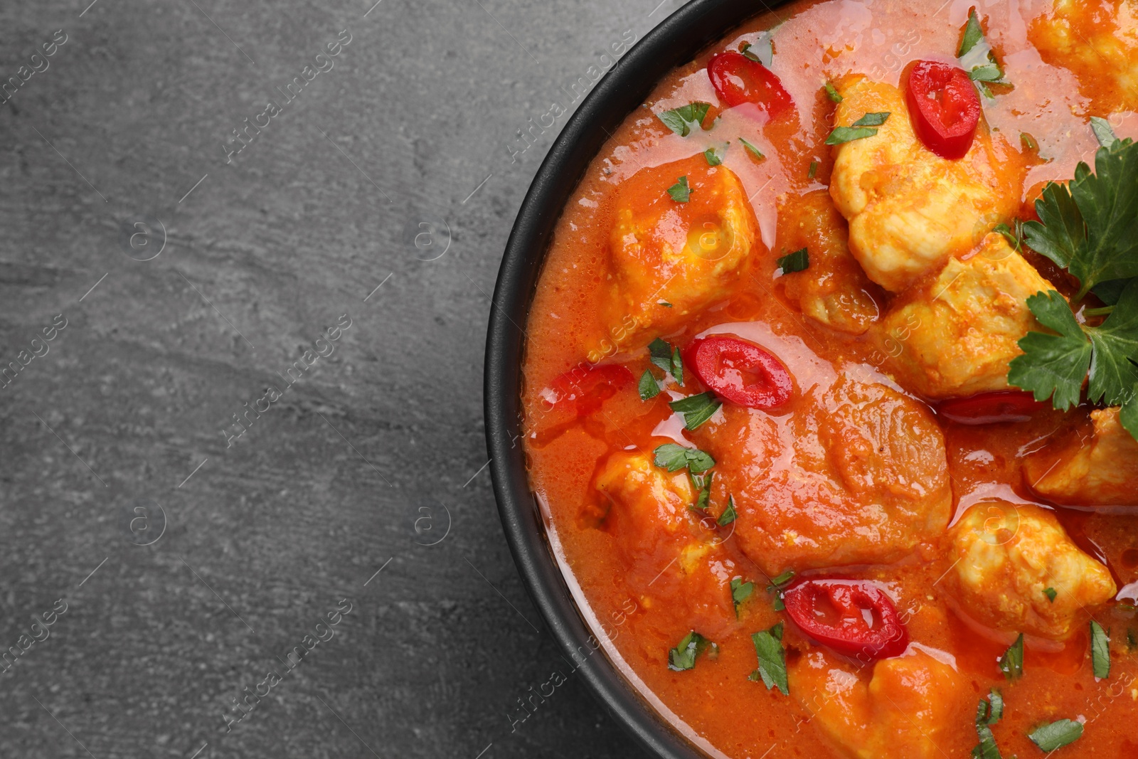 Photo of Bowl of delicious chicken curry on grey table, top view. Space for text