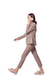 Photo of Happy young woman in formal suit talking on smartphone while walking against white background