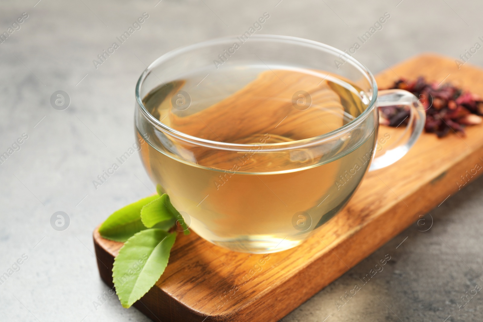 Photo of Cup of green tea and leaves on grey table, closeup