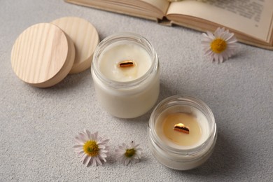 Photo of Burning scented candles and chamomile flowers on light gray textured table, above view