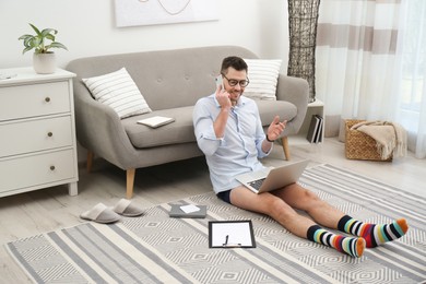 Businessman in shirt and underwear talking on phone during video call at home