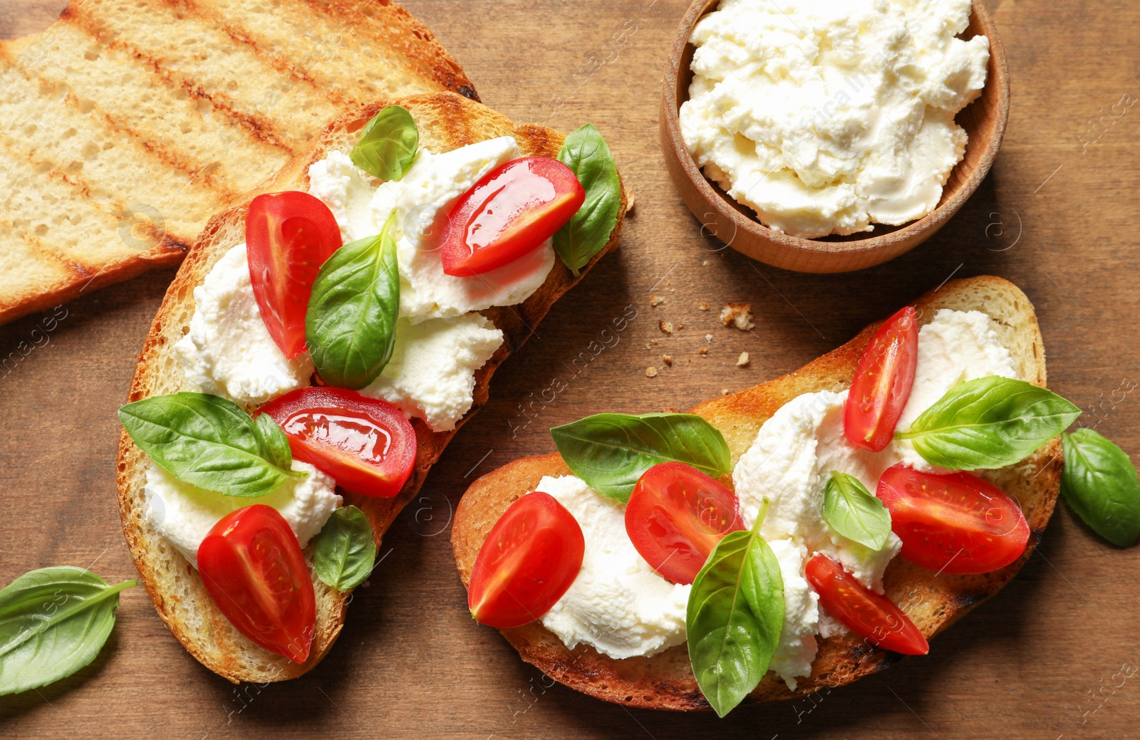 Photo of Toasted bread with tasty cream cheese and tomatoes on wooden table, flat lay