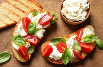 Photo of Toasted bread with tasty cream cheese and tomatoes on wooden table, flat lay