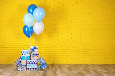 Many gift boxes and balloons near yellow brick wall. Space for text