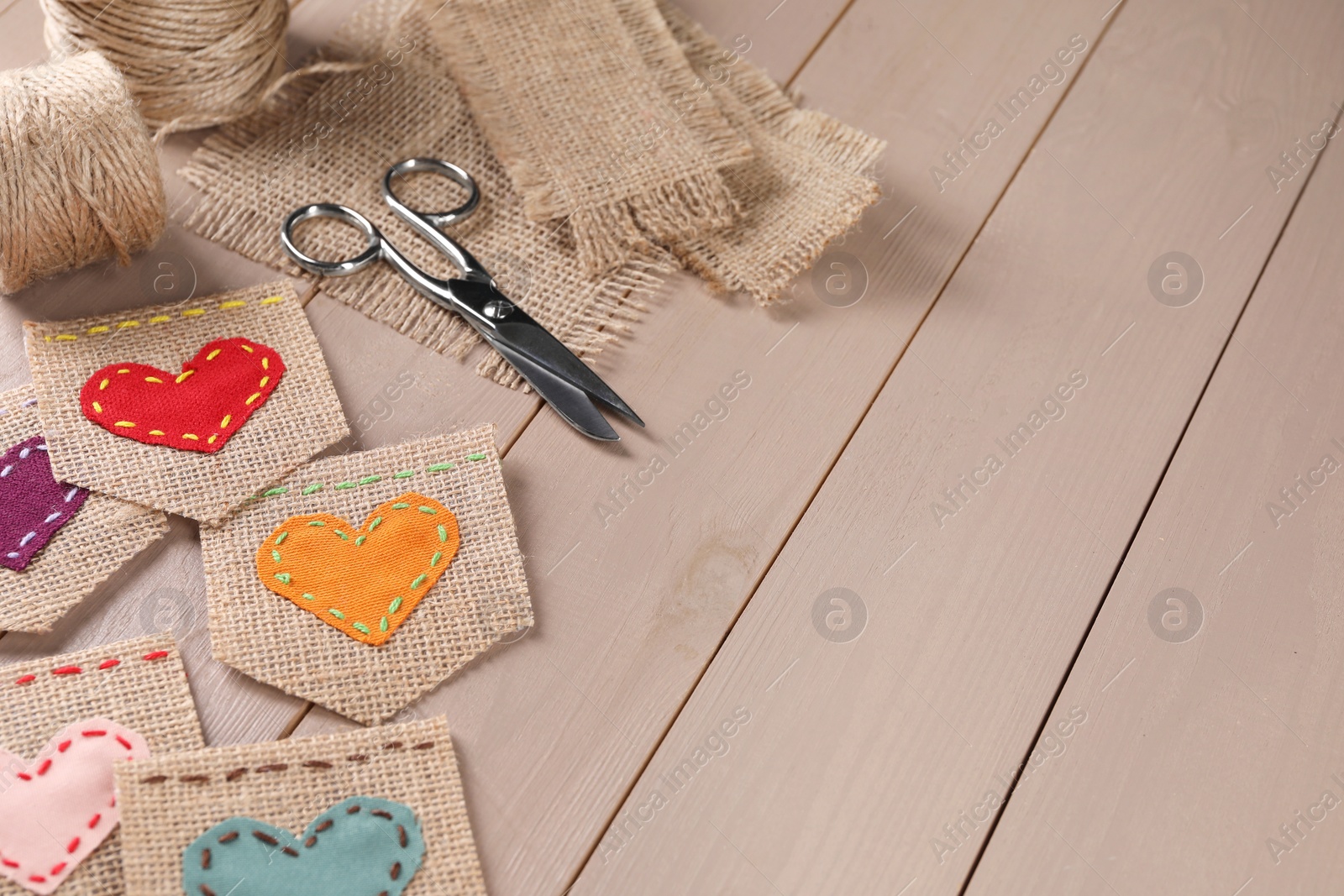 Photo of Pieces of burlap fabric with hearts and scissors on wooden table, above view. Space for text