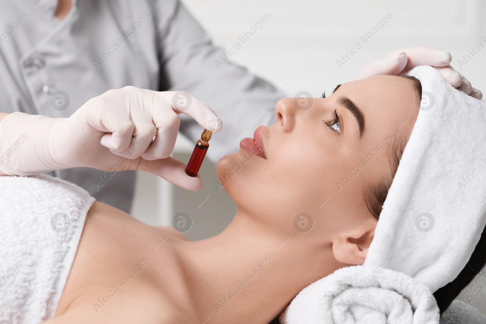 Photo of Professional cosmetologist holding skincare ampoule while working with client in clinic, closeup