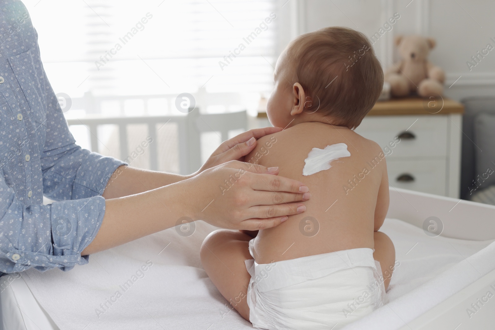 Photo of Mother applying body cream on her little baby at home, closeup