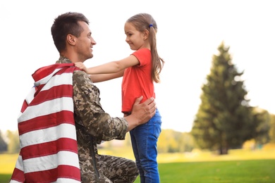 Photo of Father in military uniform with American flag and his daughter at sunny park