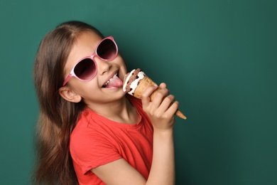 Photo of Cute little girl with delicious ice cream against color background, space for text