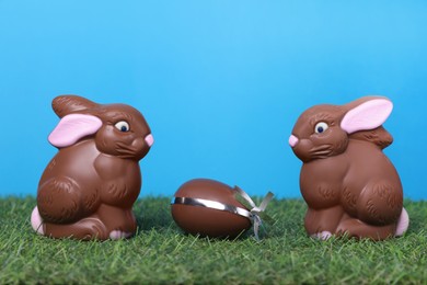 Photo of Easter celebration. Cute chocolate bunnies and egg on grass against light blue background