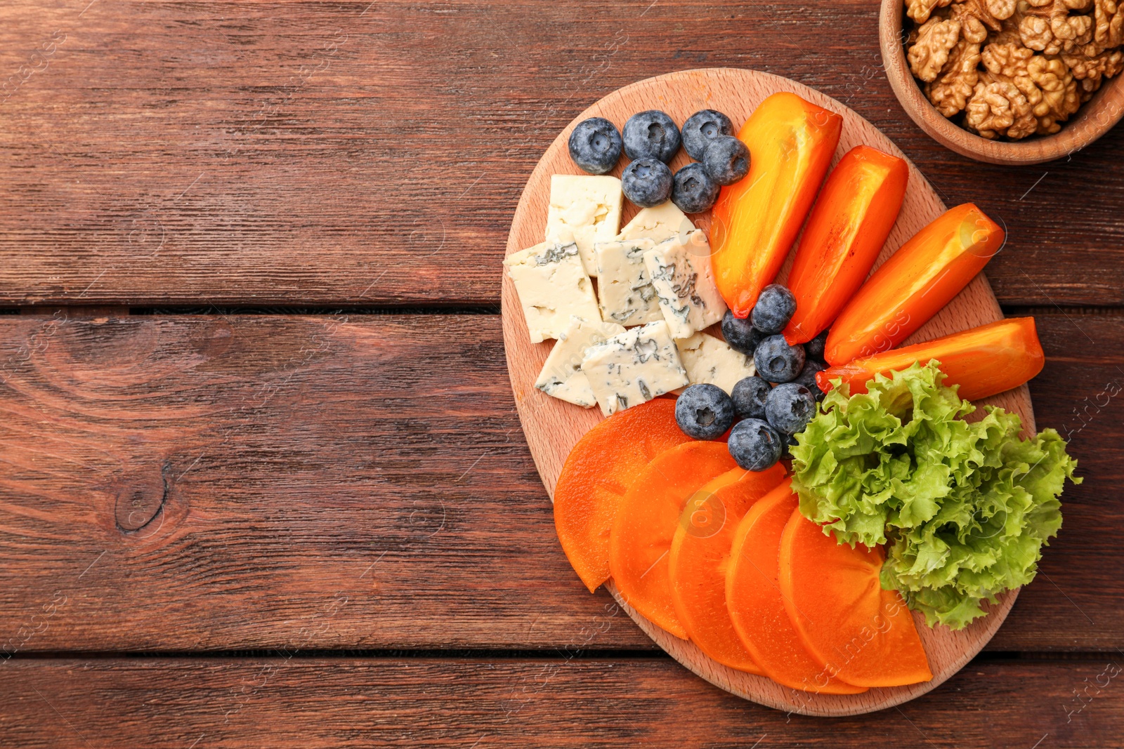 Photo of Delicious persimmon, blue cheese and blueberries on wooden table, flat lay. Space for text