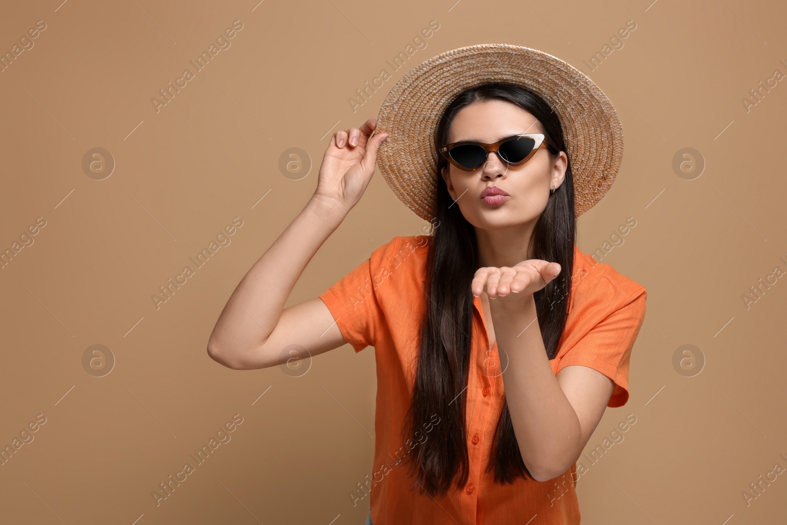 Photo of Beautiful young woman in straw hat blowing kiss on beige background. Space for text