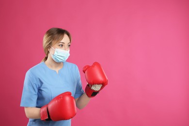 Photo of Doctor with protective mask and boxing gloves on pink background, space for text. Strong immunity concept