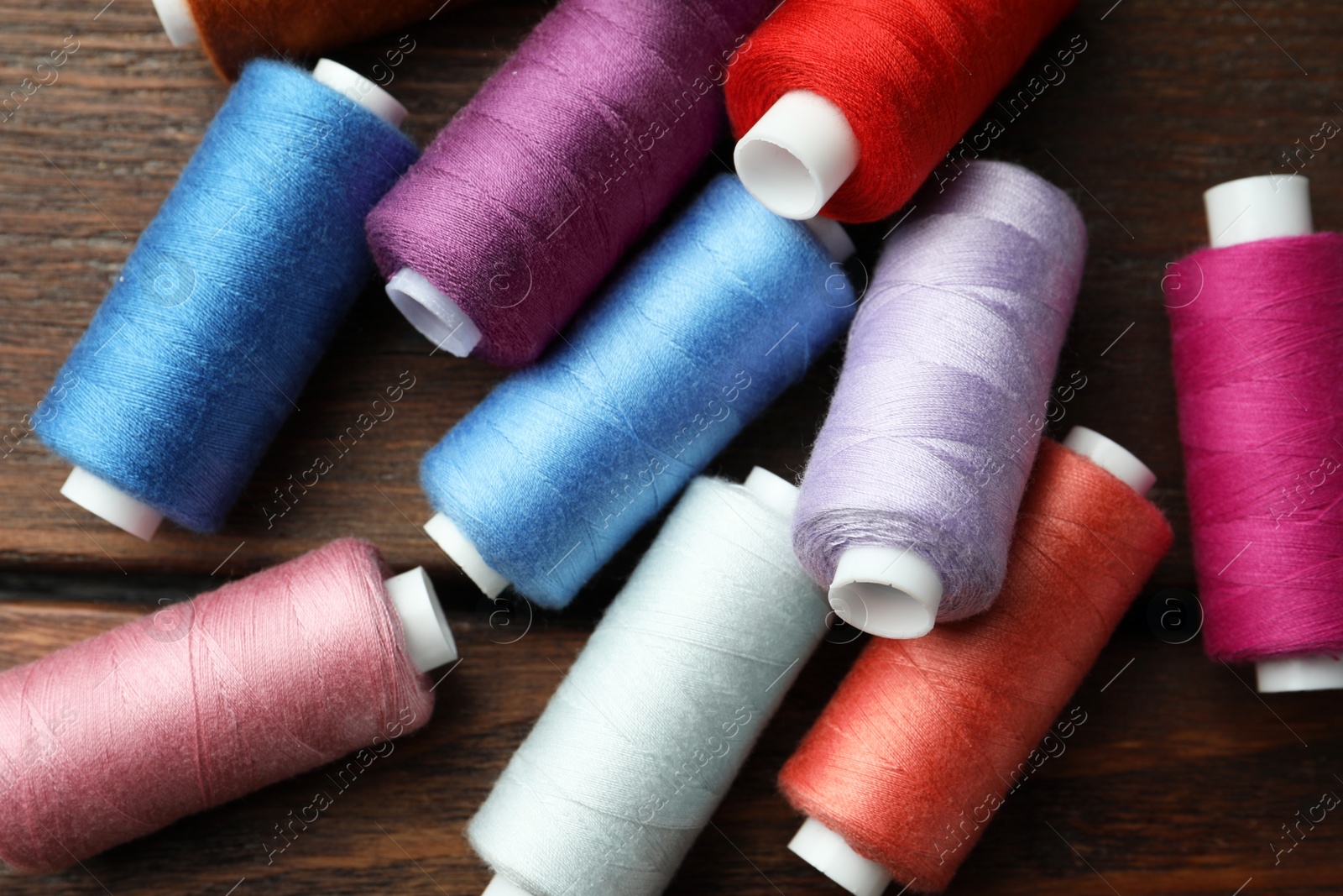 Photo of Different colorful sewing threads on wooden table, flat lay