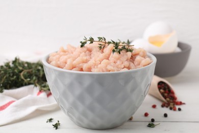 Fresh raw minced meat and thyme in bowl on white wooden table, closeup
