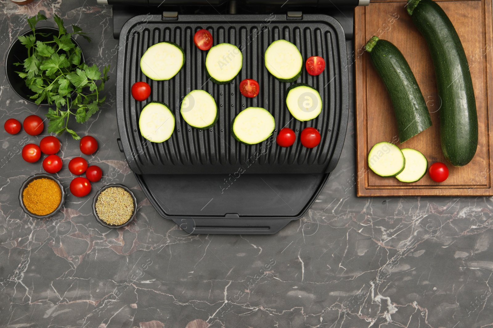 Photo of Electric grill with vegetables and spices on black marble table, flat lay. Space for text