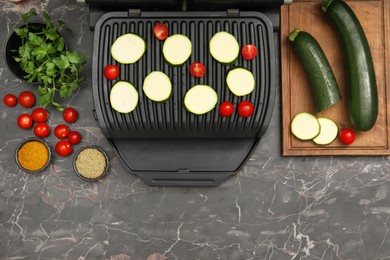 Photo of Electric grill with vegetables and spices on black marble table, flat lay. Space for text