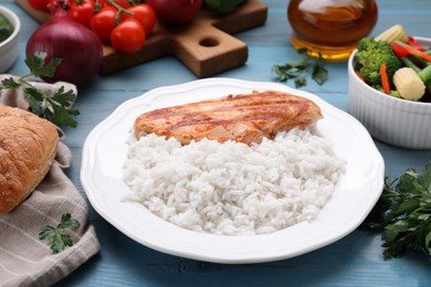 Photo of Grilled chicken breast and rice served with vegetables on light blue wooden table
