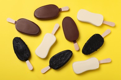 Photo of Different glazed ice cream bars on yellow background, flat lay