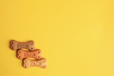 Photo of Bone shaped dog cookies on yellow background, flat lay. Space for text