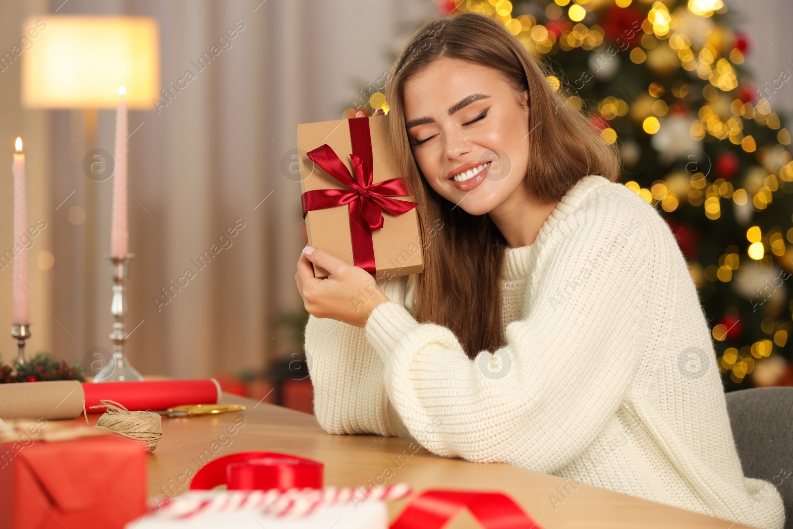 Photo of Beautiful young woman with Christmas gift and decor at table in room