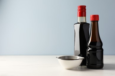 Photo of Bottles and bowl with soy sauce on white table, space for text