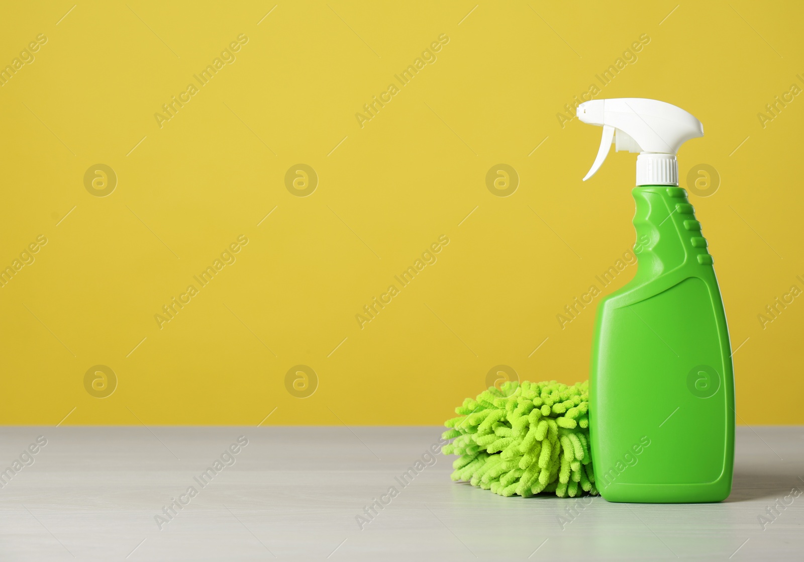 Photo of Bottle of cleaning product and fluffy microfiber cloth on light table. Space for text