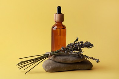 Photo of Bottle of face serum, spa stones and lavender flowers on yellow background