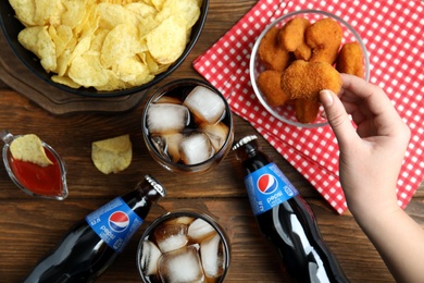 Photo of MYKOLAIV, UKRAINE - FEBRUARY 16, 2021: Woman eating chicken nuggets at wooden table with Pepsi, top view