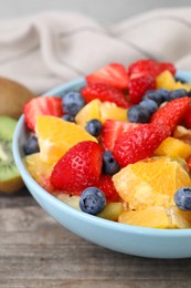 Delicious fresh fruit salad in bowl on wooden table, closeup