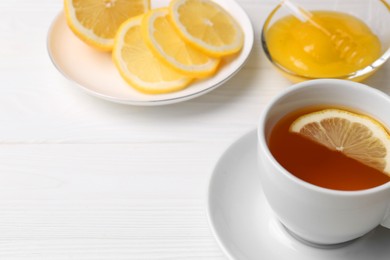 Cup with delicious immunity boosting tea, lemon and honey on white wooden table, space for text