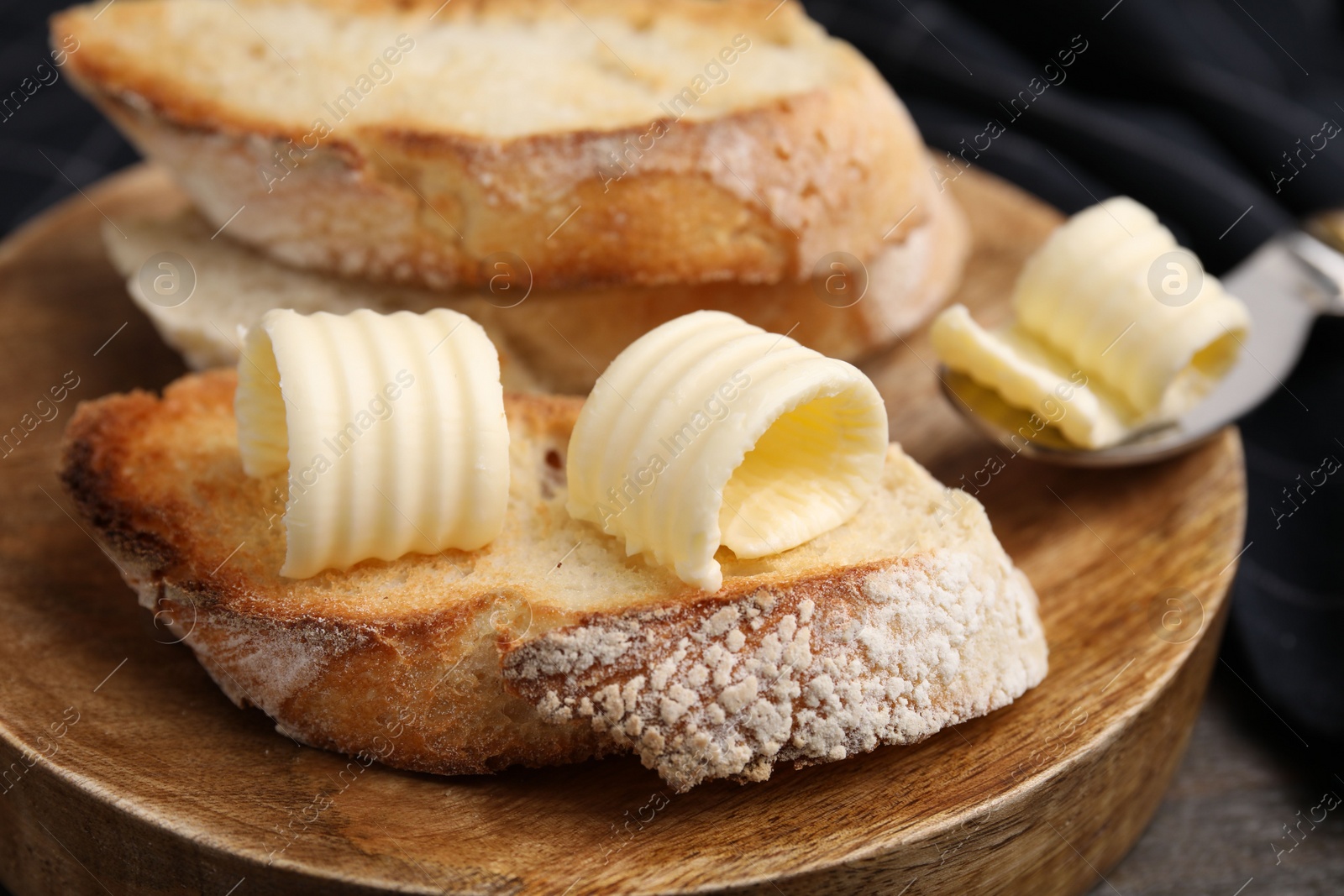 Photo of Tasty butter curls and slices of bread on wooden table, closeup