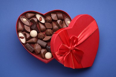 Photo of Heart shaped box with delicious chocolate candies on blue background, top view