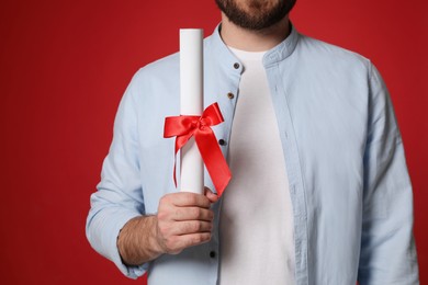 Student with diploma on red background, closeup