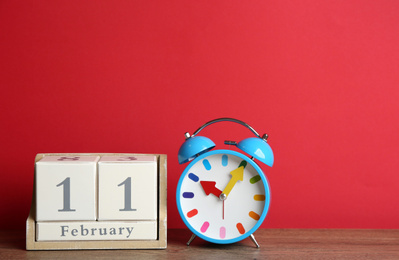 Wooden block calendar and alarm clock on table against red background