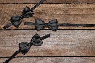 Photo of Stylish black bow ties on wooden background, flat lay. Space for text