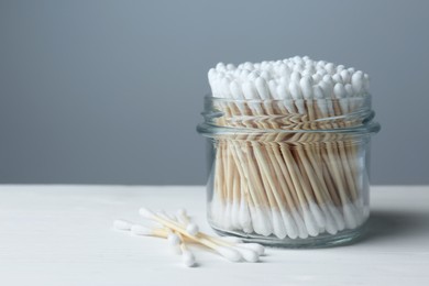 Many cotton buds on white wooden table against grey background, space for text